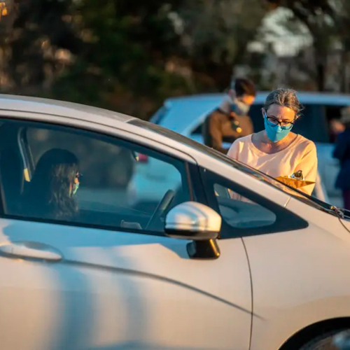 A health care worker taking information from a woman in a car in line for a vaccine.